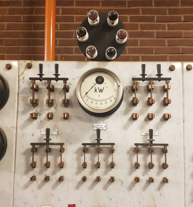 Gammalt kontrollpanel för generator med knivbrytare, emaljerade skyltar, kW-mätare och släpringar.