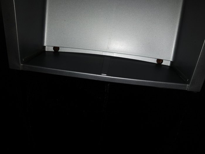 Närbild på skruvar bakom en grå spillbricka i ett plasthus, svart bakgrund.