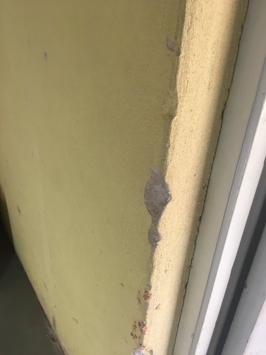 Källarvägg med gul färg som flagar av och visar betongunderlaget vid hörnet.