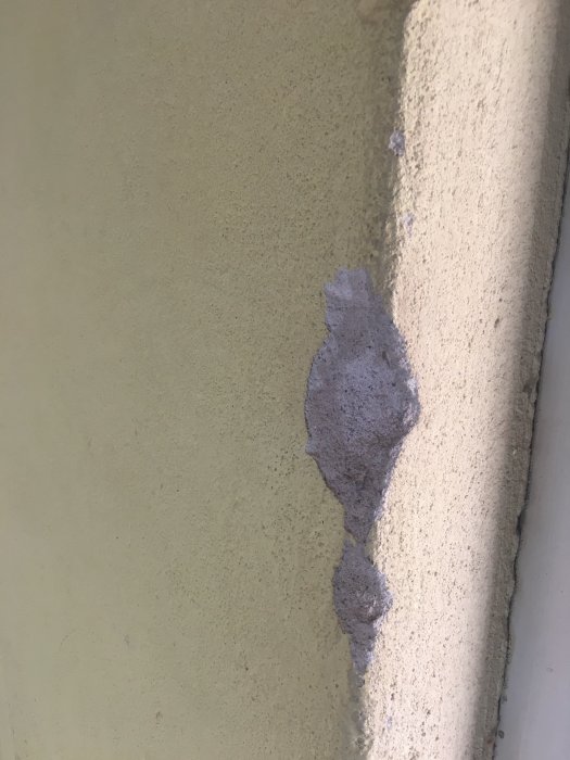 Betongvägg med gul färg och en fläck där färg/spackel är borttaget, exponerar underlaget.