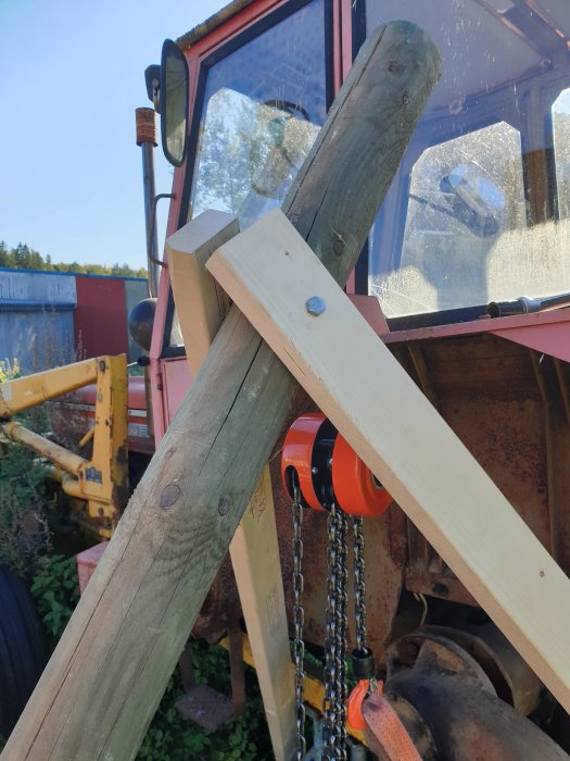 Hemmagjord lyftanordning med tjock grindstolpe och 2x4 reglar, försedd med lyftblock, framför traktor.