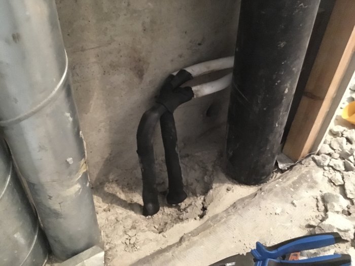 Rörinstallation i betonggolv under badrumsrenovering med synligt borrhål och svarta rör.