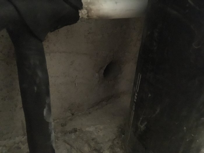 Badrumsrenovering med svart rör nära borrhål i betongvägg som skapar undertryck och behov av reparation.