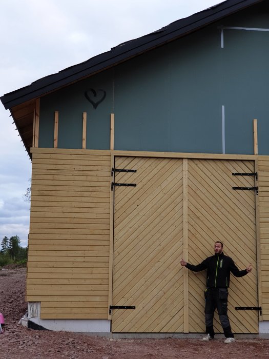 Person står mellan stora träportar med lång gängstång och tunga gångjärn på en byggplats.