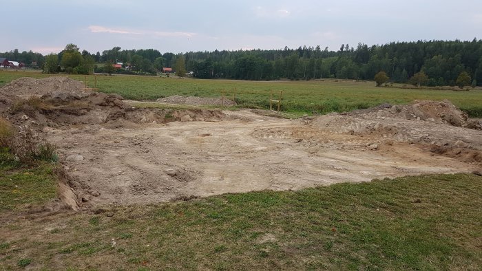 Förberedd husgrund med utgrävda marker, armeringsjärn och kantelement på en byggplats.