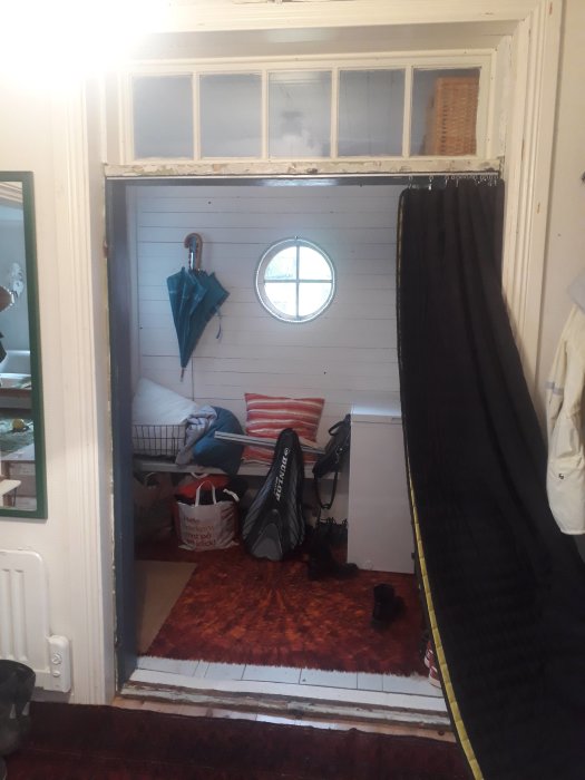 Ett kaotiskt hallutrymme med skor, golfbag, paraply och kläder strödda runtomkring, och en rund fönsterruta.