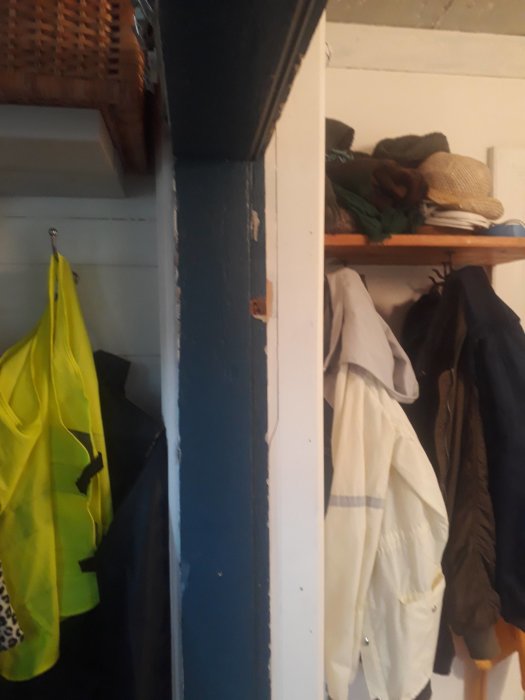 En halvfärdig trävägg målad i blått med en hängande hylla och krokar för ytterkläder.