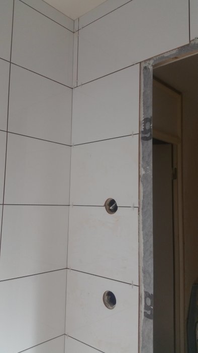 Kakelarbete i hörn av badrum med synliga ojämnheter och kakelklipp kring rörgenomföringar.