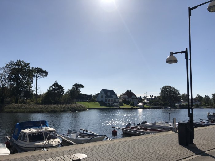 Solsken över en småbåtshamn med båtar vid bryggan och traditionella hus i bakgrunden.