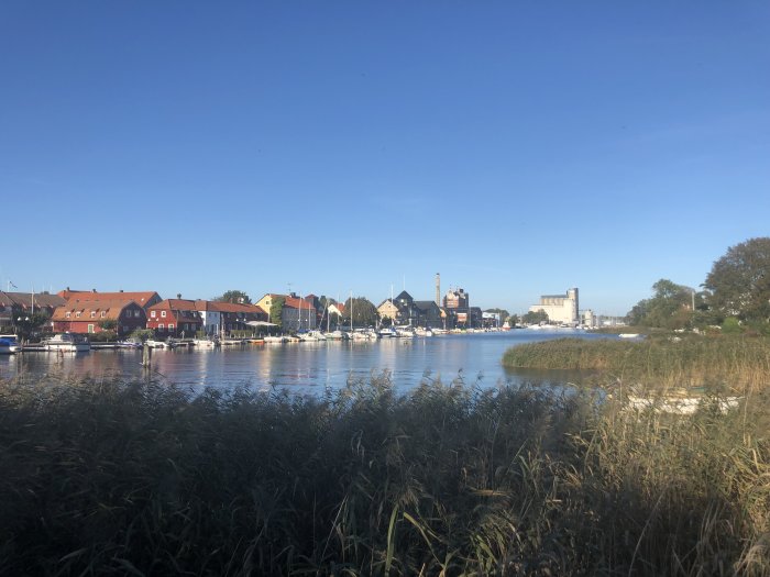 Vy över en flod med båtar och färgglada hus mot en klarblå himmel, oklart vilken ort.