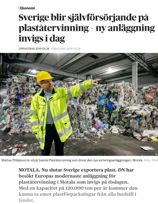 Man i säkerhetskläder pekar på en stor hög av komprimerade plastförpackningar i återvinningsanläggning.