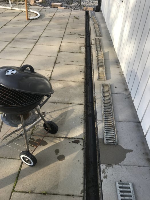 En rengjord markränna vid en terrass med borttagna galler och en kolgrill i förgrunden.