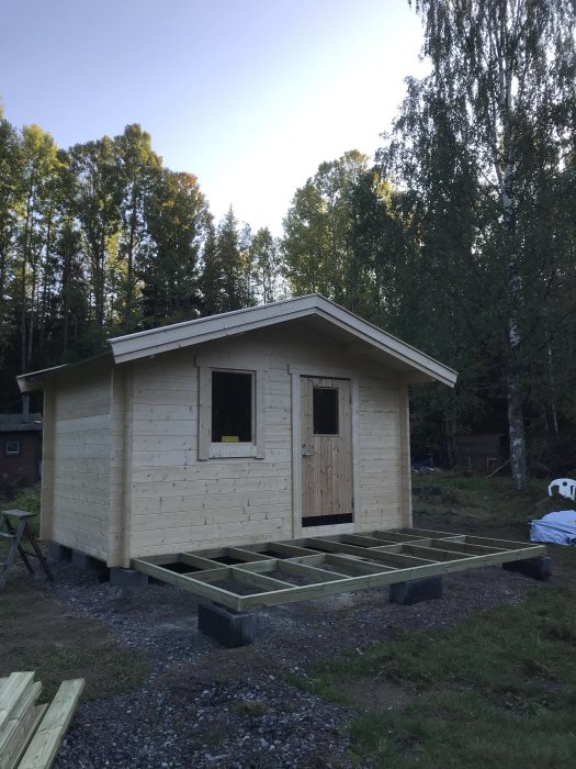 En nybyggd koja med träbeklädnad och fundament under konstruktion, omgiven av skog.