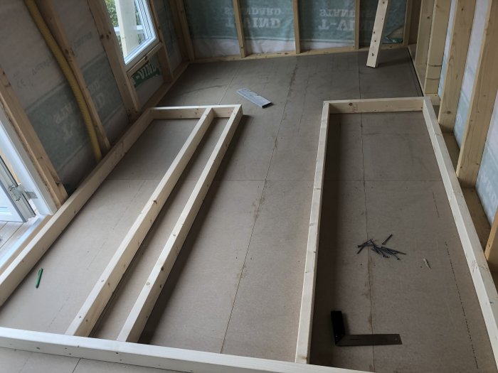 Uppmätta träreglar ligger på golvet för planering av en bastu, med isolering synlig på väggarna.
