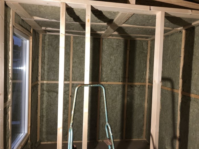 Reglade väggar och tak i en bastu under konstruktion, isolering synlig, ingen takbelysning.