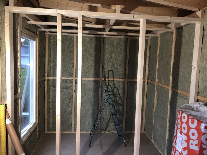 Påbörjad bastukonstruktion med reglat tak och väggar isolerade med stenull, inga taklampor, en stege i bakgrunden.