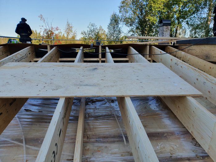 Konstruktion av nytt tak med träbalkar och plywood under pågående byggarbete.