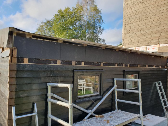 Hus under renovering med nytt tak under konstruktion, stående ställning och träd i bakgrunden.