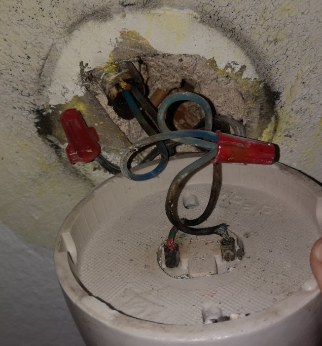 Öppnat lamputtag med ärgade och brända elektriska sladdar och ojämnt målad vägg runtomkring.