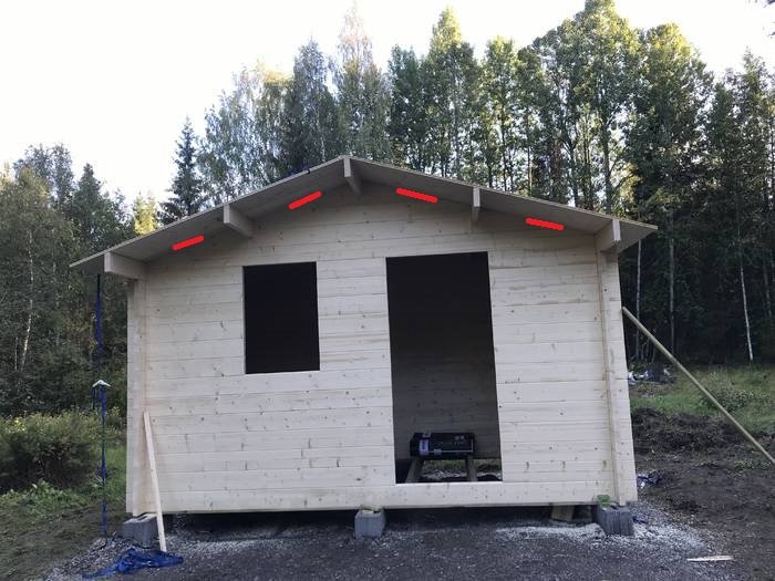 Obehandlad träfasad på en fristående byggnad med markerade områden för ventilation längs takfoten.