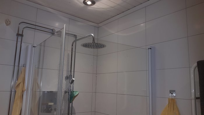 Vitkaklat badrum med duschhörna, takdusch och plattsättning efter beskriven teknik.
