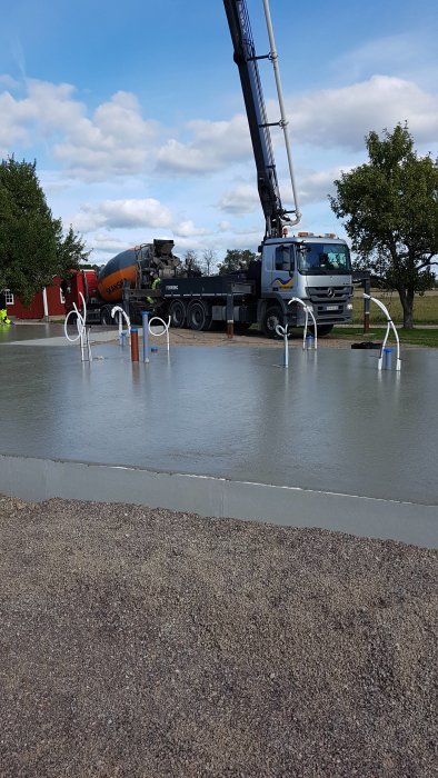 Nyggjuten betonggrund med framstående rör och lastbil med betongpump.