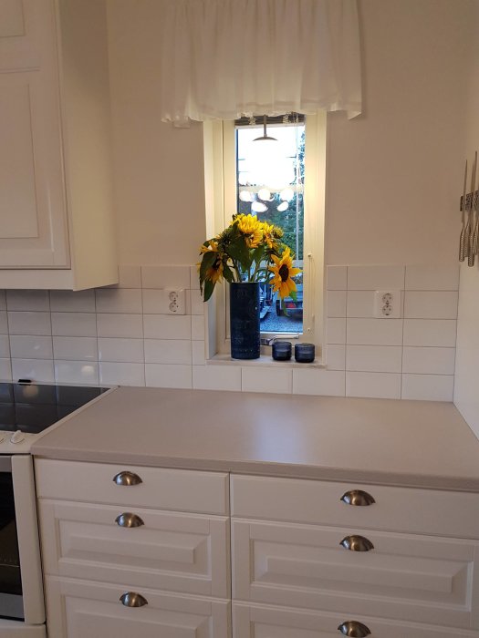Kök med asymmetriskt placerade eluttag och ocentrerat kakel runt fönster, vit inredning.