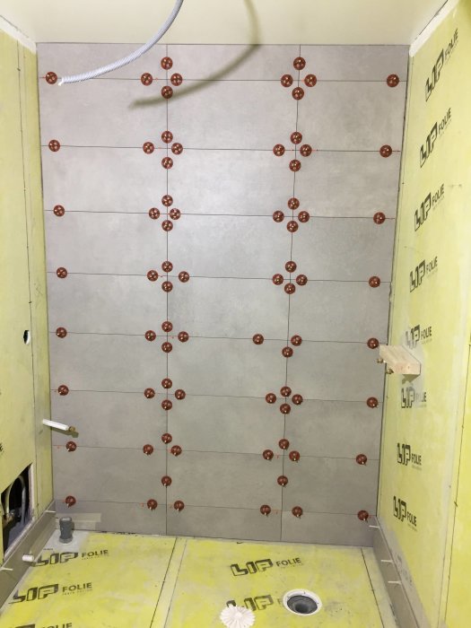 Badrumsvägg under kakling med asymmetrisk placering av 30x60 cm plattor och ojämn kapning.
