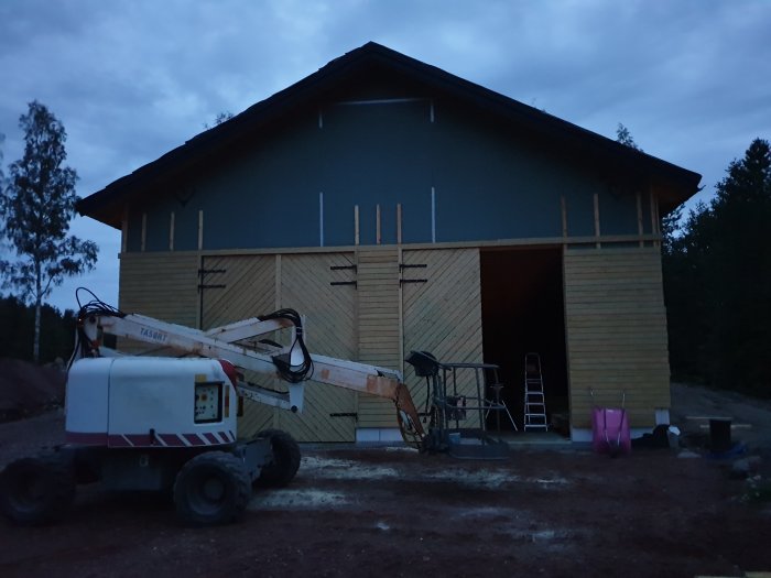 En nybyggd byggnad i skymningen med tre installerade garageportar och byggutrustning i förgrunden.