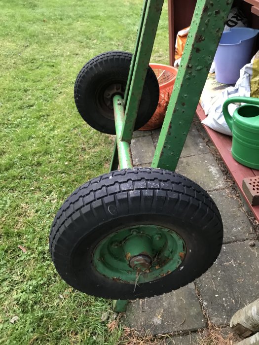 Tungt litet släpvagnschassi med två hjul, använt bakom gräsklippare, står på gräs.