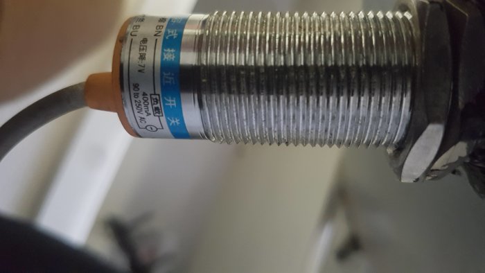 Närbild av en anordning med gängad metallstång och etikett, troligen en del av en bygginstallation.