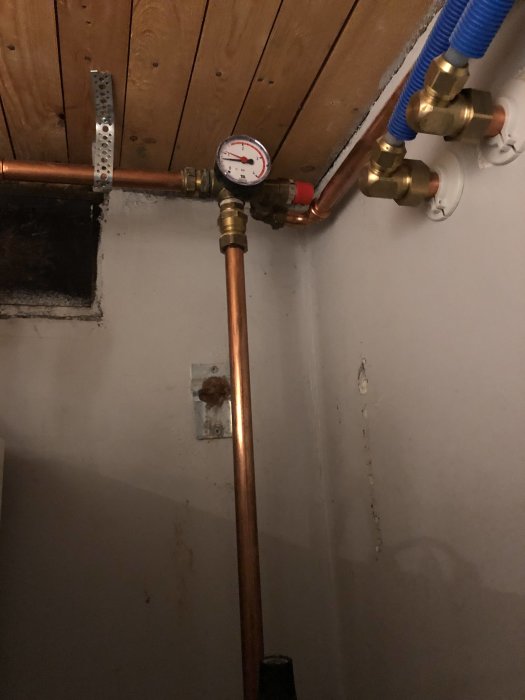 Installation av manometer på kopparledning för att kontrollmäta tryck med anslutna kranar och slangar mot en trävägg.