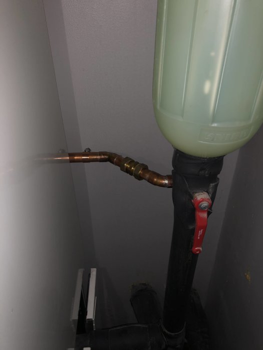 Kopparrör anslutna till en genomskinlig behållare med en röd kran för att kontrollmäta och byta tryck.