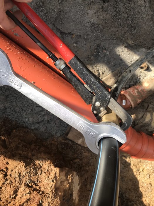 Närbild av installation av rör med PRK-nyckel och kopplingar i ett grävt schakt.