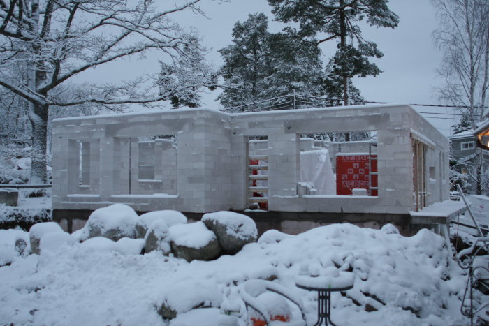 En halvfärdig husvägg av murblock täckt av snö vid en byggplats.