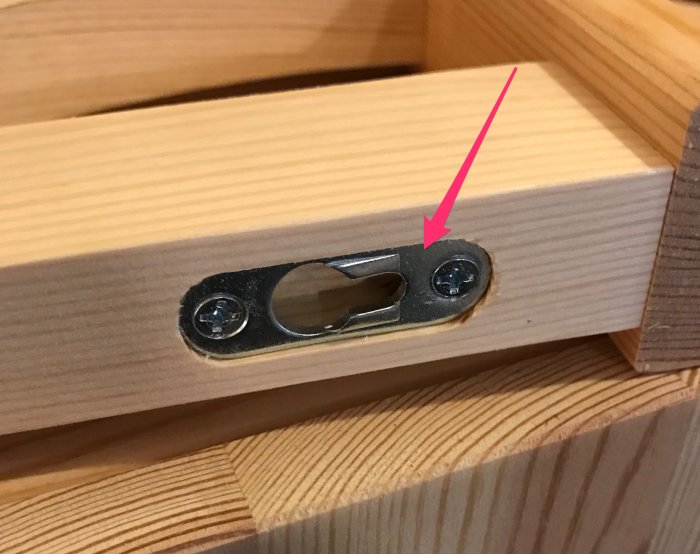 Upphängningsbeslag på träyta med skruvar, markerat med rosa pil.