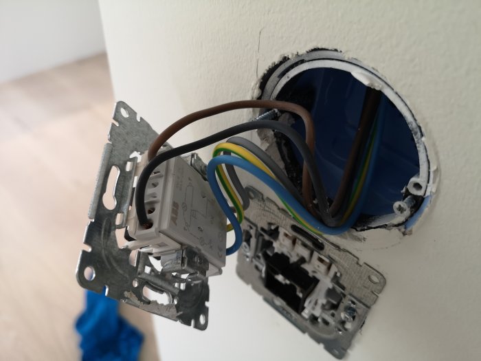 Öppet eluttag i vägg med exponerade ledningar och kopplingsdosa redo för installation av dosdimmer.