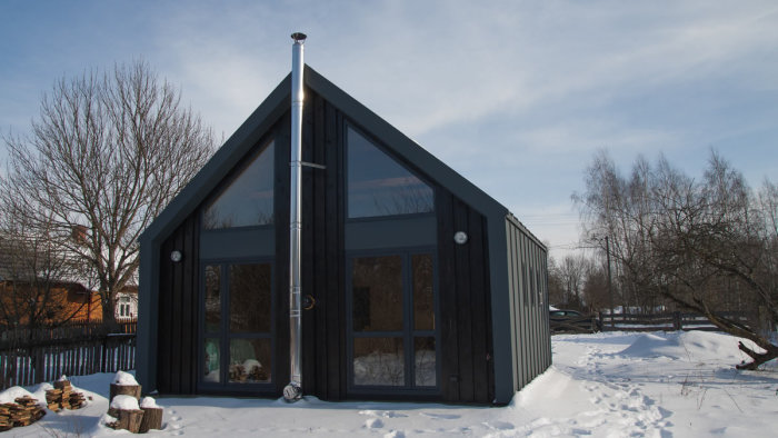 Svart, spetsig husfasad med stora fönster mot en snöig omgivning som symboliserar modern design och smart utrymmesanvändning.