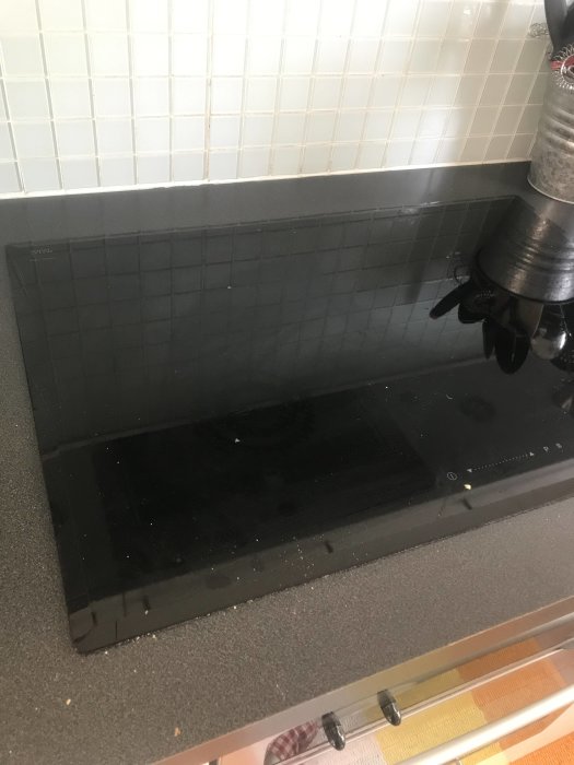 Köksbänk med en inbyggd svart Schott Ceran häll mot en kakelvägg, ovanpå en IKEA bänkskiva.