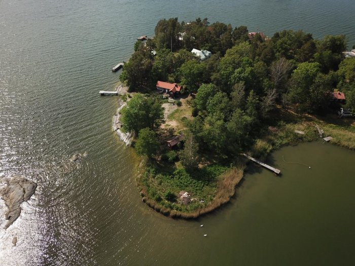 Flygbild av ett hus på en grön klippö omgiven av sjövass nära Vaxholm.