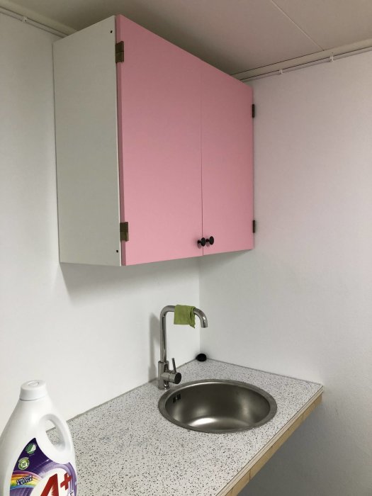 Renoverad hörna i källare med nyinstallerad bänkskiva, tvättho, blandare och rosa skåp.