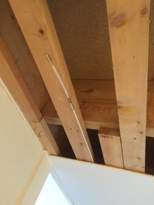 Bild av ett öppet mellanbjälklag med synliga träbjälkar och borrade hål för elinstallationer.
