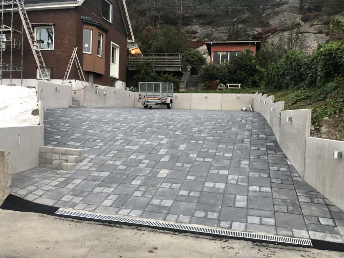 Nyrenoverad utomhuspatio med kullerstensliknande plattor och murade sittplatser under uppbyggnad.