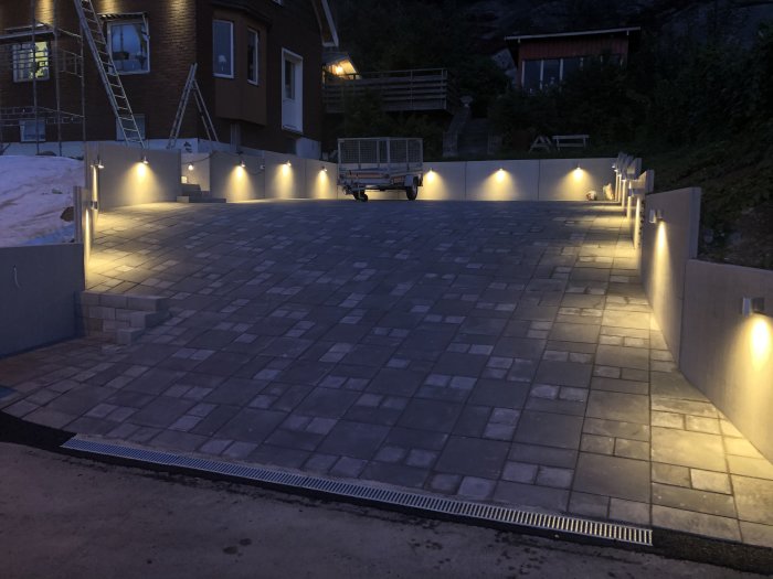 Upplyst stenlagd uteplats på kvällen med inbyggda LED-spotlights i väggen.