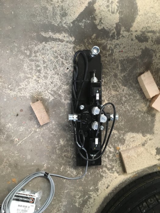 Hydraulisk utrustning med slangar och spakar på ett smutsigt betonggolv.