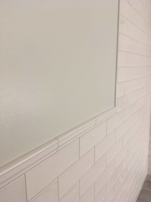 Vit vägg med list och vit kaklad del, ren och modern inredningsdetalj.