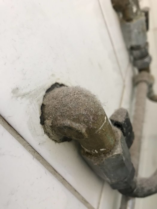 Vattenledning med en 90-gradersböj ur väggen i ett badrum, ämne för installation av blandare.