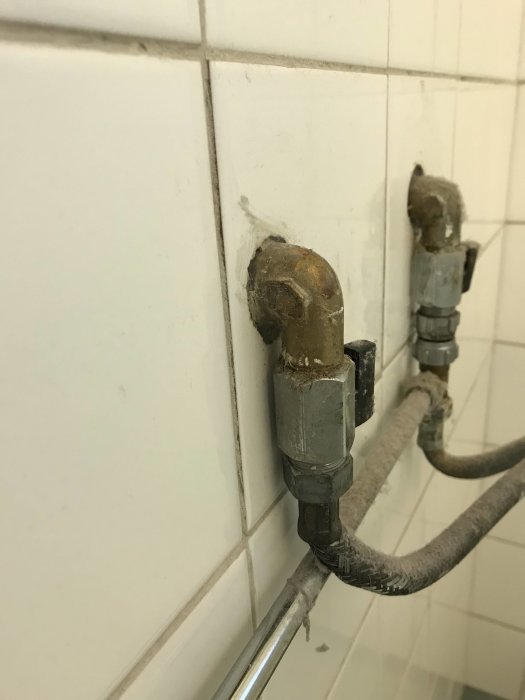 Väggmonterade vattenrör med 90-gradersböj i ett badrum för duschkabinanslutning.