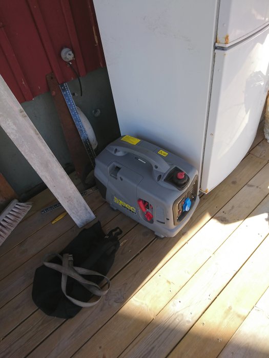 Meec Tools bensinelaggregat modell 740034 placerat på trägolv bredvid kylvit skåp och svart väska.
