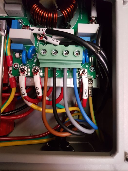Detaljbild av insidan av elskåpet med färgkodade kablar anslutna till terminaler och skyddstransformator i en solcellsanläggning.